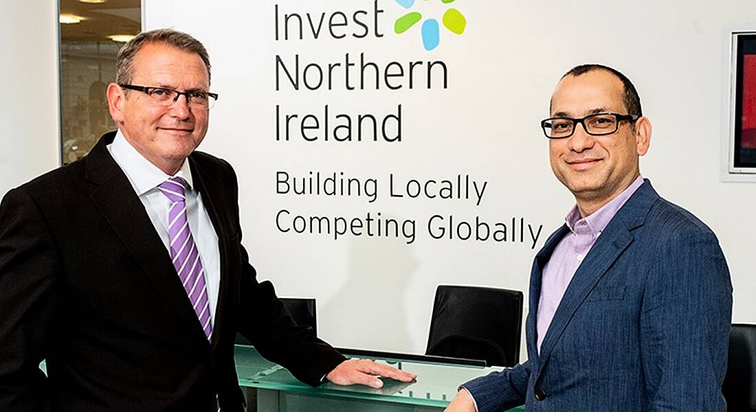 View of two men in business attire standing in front of wall with Invest NI logo.