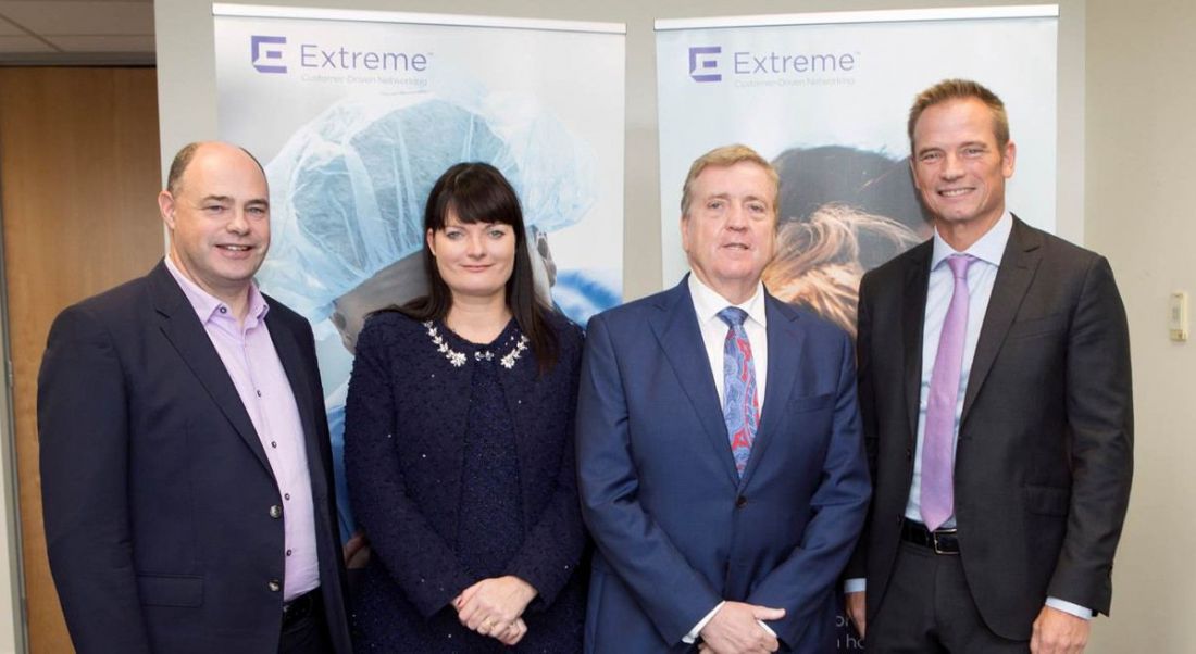 View of people in business attire standing in front of purple Extreme Networks logo.