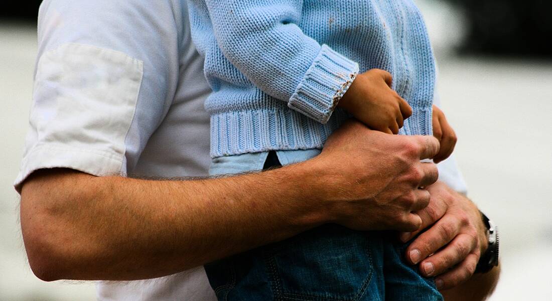 Photograph of a man holding a small child, showing only the midriff.