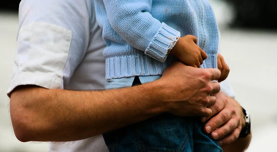 Photograph of a man holding a small child, showing only the midriff.