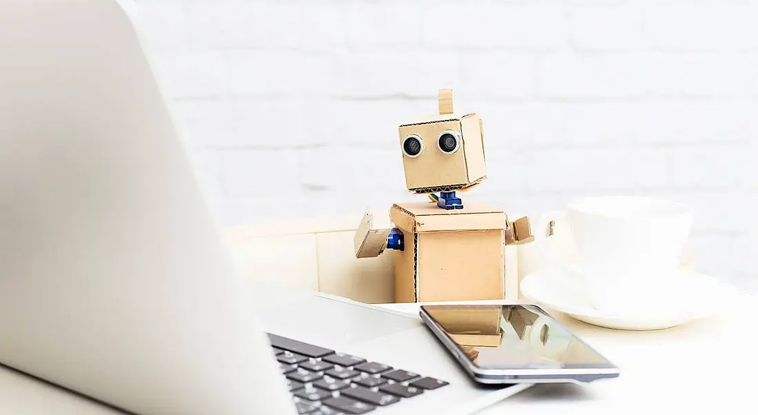 Robot sitting at a table and drinking coffee while working on a computer.