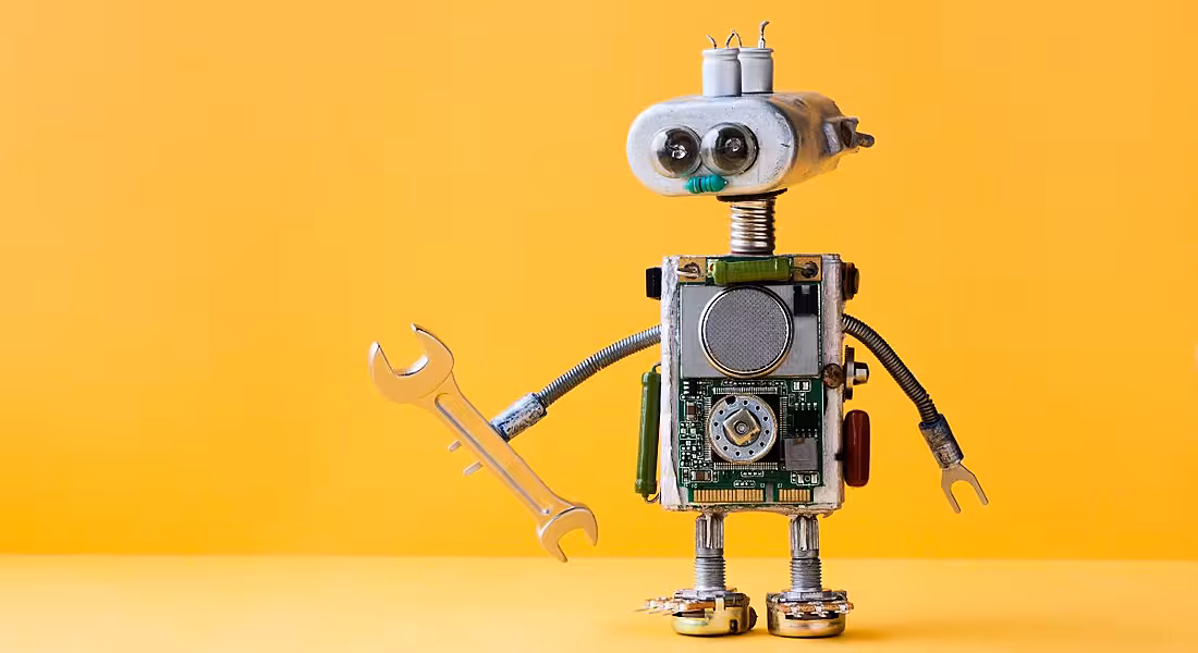 Small toy robot holding a spanner against a yellow background.