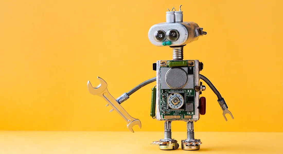 Small toy robot holding a spanner against a yellow background.