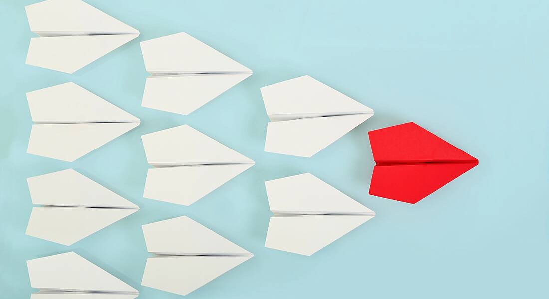 Red paper plane leading white ones, all placed against a light blue background.