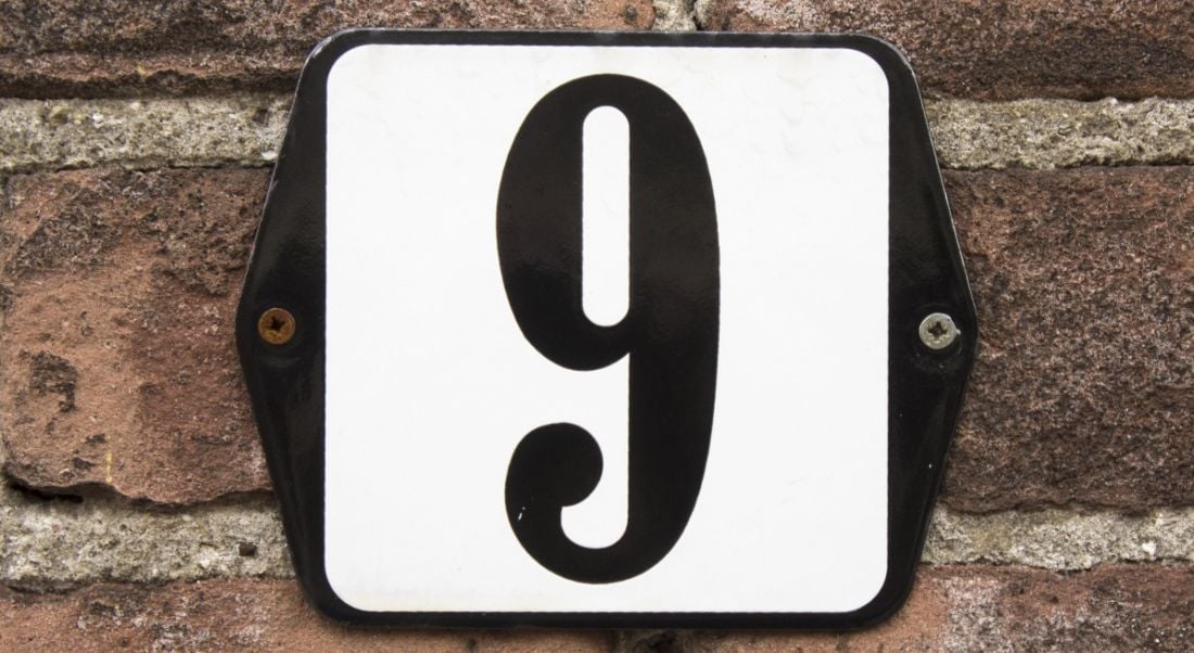 Enamelled number sign on the front of a house, displaying the number nine in black lettering on a white background.