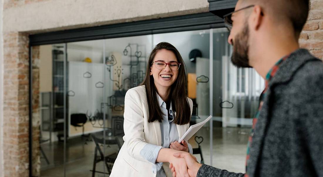 A woman shaking hands with a man and smiling. They are starting a very positive onboarding process.