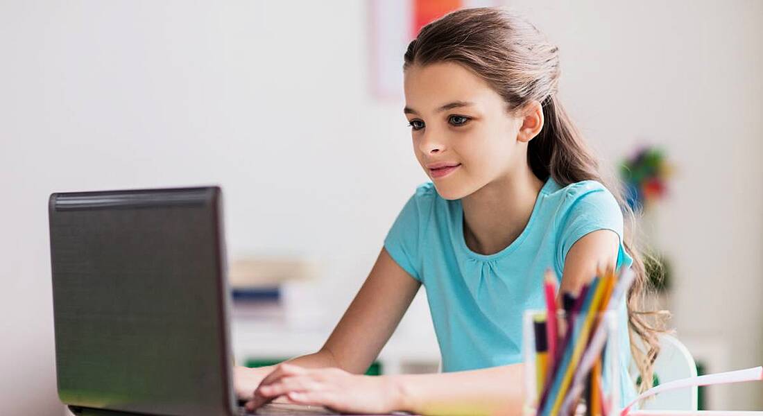 A young girl sitting at desk with a laptop in front of her, possibly playing a game about cybersecurity.