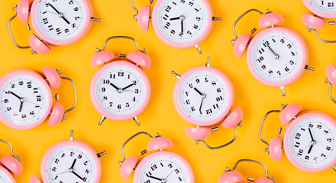 A series of pink old-style alarm clocks showing various times evenly spaced out against a yellow background.