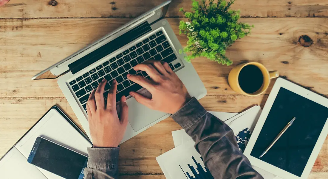 Above view of man’s hands tapping away on a laptop, concept of a side hustle.