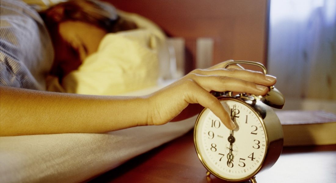 view of a sleeping person with their hand slapping an alarm that is shocking them into consciousness.