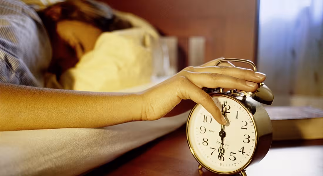 view of a sleeping person with their hand slapping an alarm that is shocking them into consciousness.