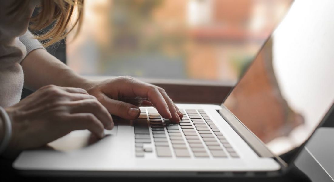 Side view of a woman’s hands resting on a laptop as she works. Tendrils of her hair are hanging down into the shot.