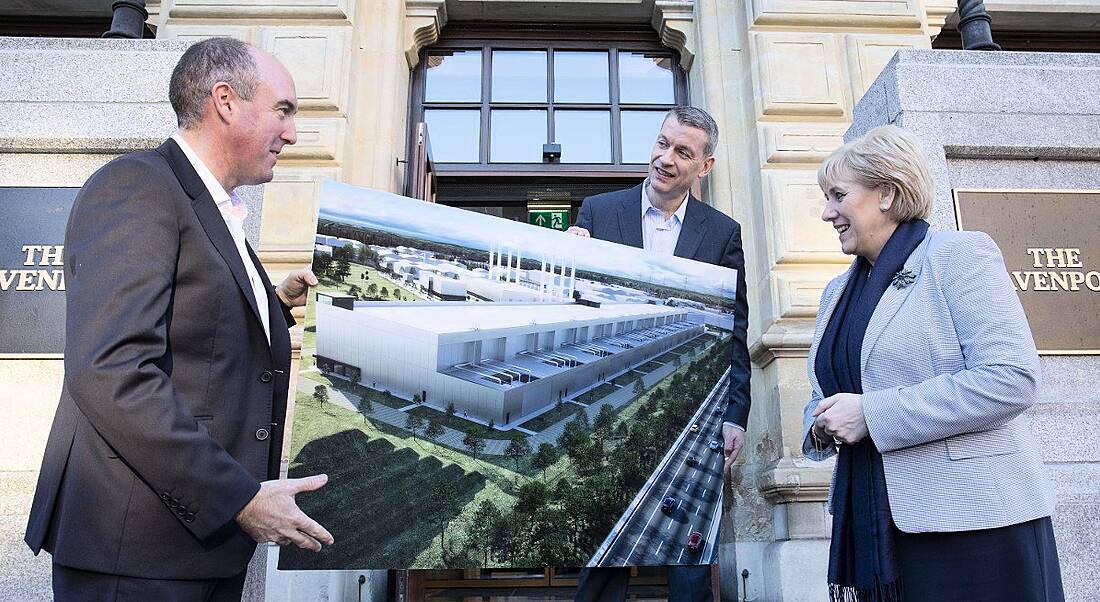 View of three middle aged people bundled in scarves and coats loosely holding up a large printout of a data centre.