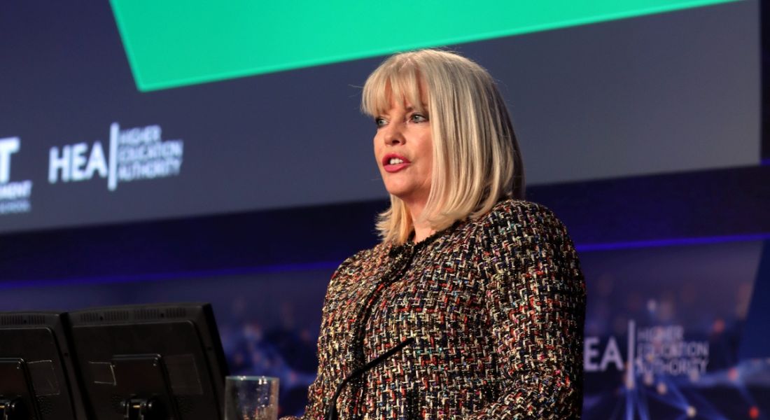 A blonde, middle-aged woman speaking at an future of work event in front of a screen. She is discussing lifelong learning.