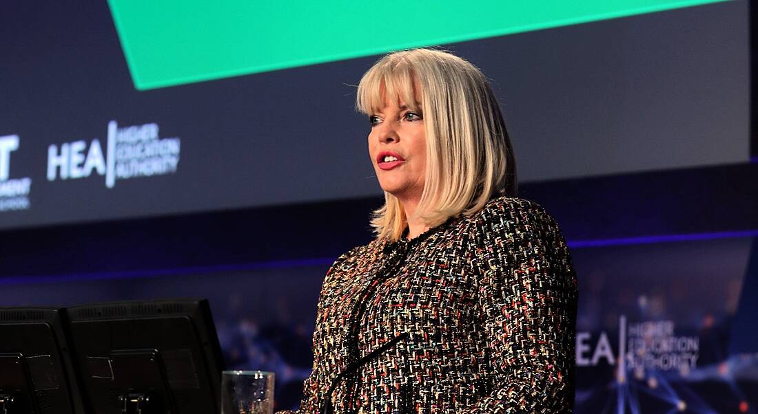 A blonde, middle-aged woman speaking at an future of work event in front of a screen. She is discussing lifelong learning.