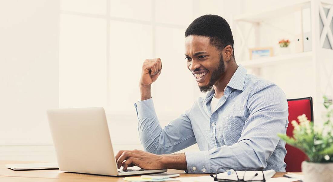 An excited man on a laptop with one fist in the air cheering. He’s excited about getting a new job.