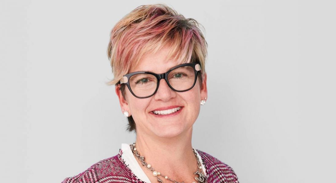 A middle-aged woman with short blonde hair flecked with pink, with black glasses, smiling at the camera. She’s the HR head of ServiceNow.