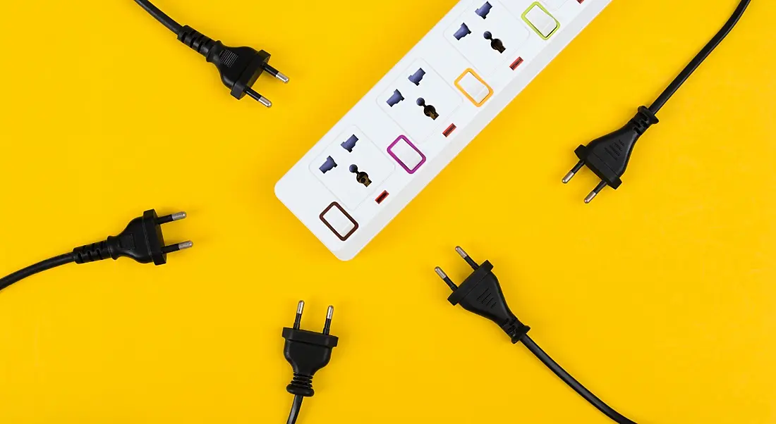 An extension cord lies on a bright yellow background with a bunch of plugs not plugged in. It represents digital wellbeing.