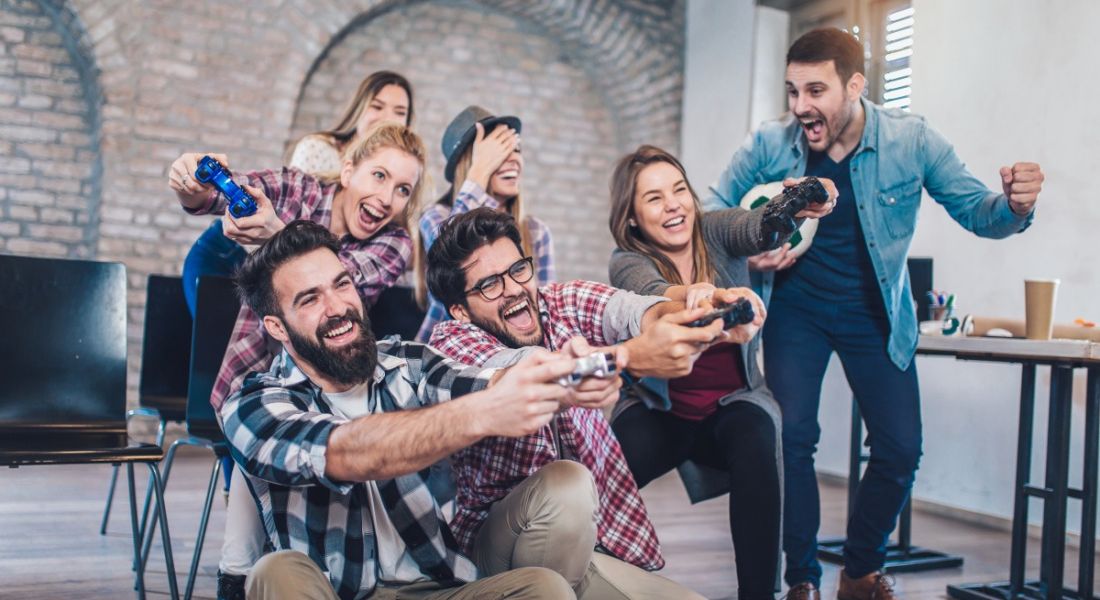 Diverse group of workers playing video games in an office and cheering with excitement.