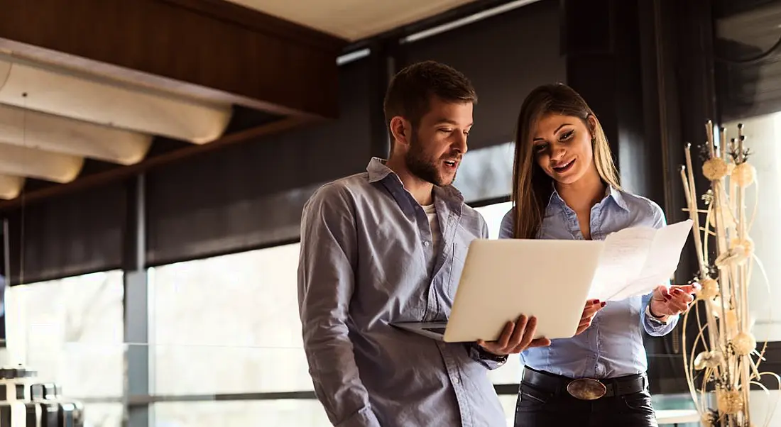 Two young employees in a well-lit office peering thoughtfully at the same file.