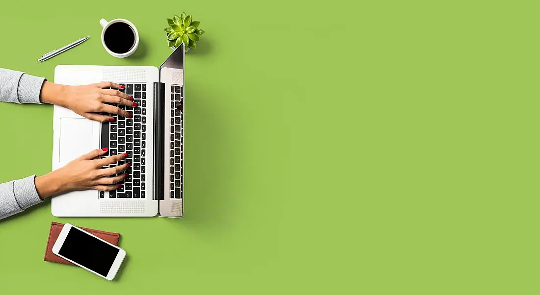 Two hands reaching out to tap on a laptop keyboard against a bright green background.