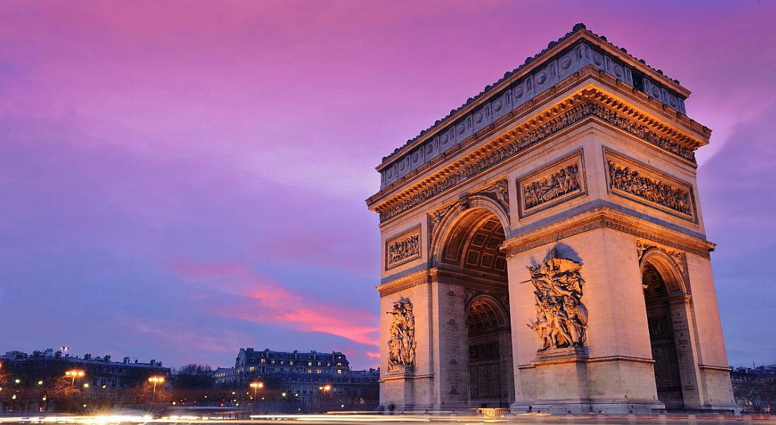 A view of the Arc de Triomphe in Paris against a purple twilight, illuminated by street lights.