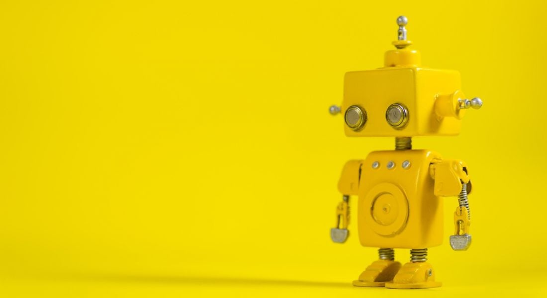 A little yellow toy robot looking askance against a bright yellow background.