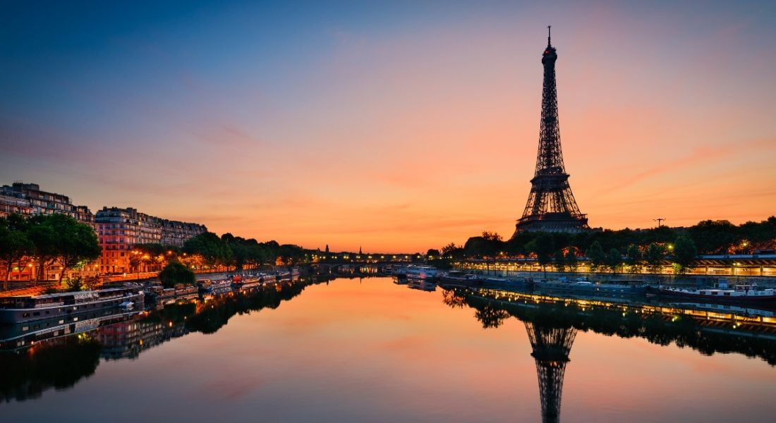 A view of the Eiffel tower and the Seine in Paris at sunrise, which fills the dark blue sky with orange.