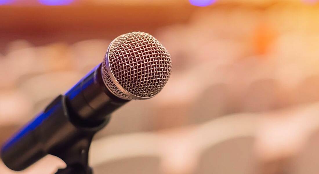 View of a microphone on a stand with a blurred out conference room in the background.