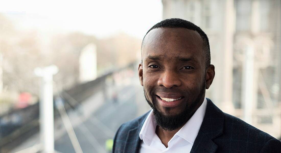 A man wearing a suit with a gleaming white smile looking up straight at the camera.