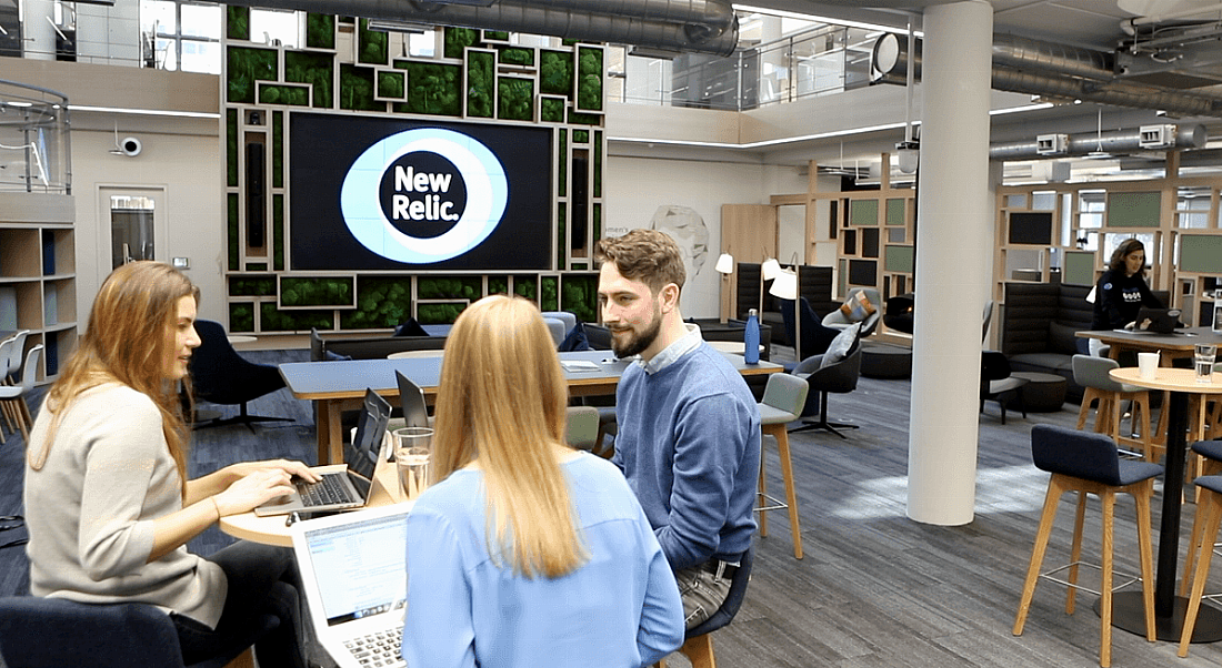 A central collaboration space in the New Relic office. Three employees in the foreground sit together chatting.