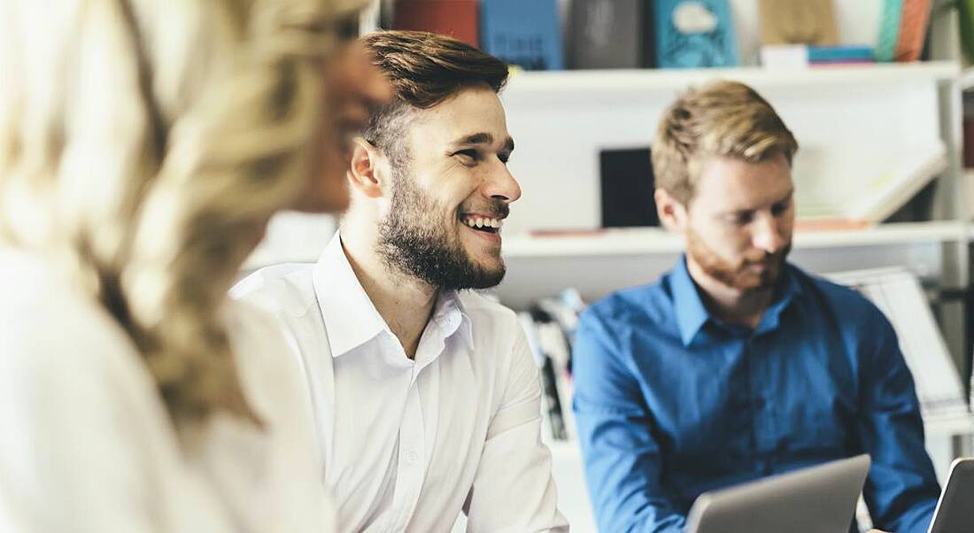 A crowd of employees laughing and talking in casual suits around a table, using their soft skills to work together.