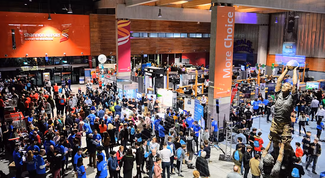 Overhead shot of a large crowd of people gathered in Shannon Airport departures hall among exhibition stands and displays.
