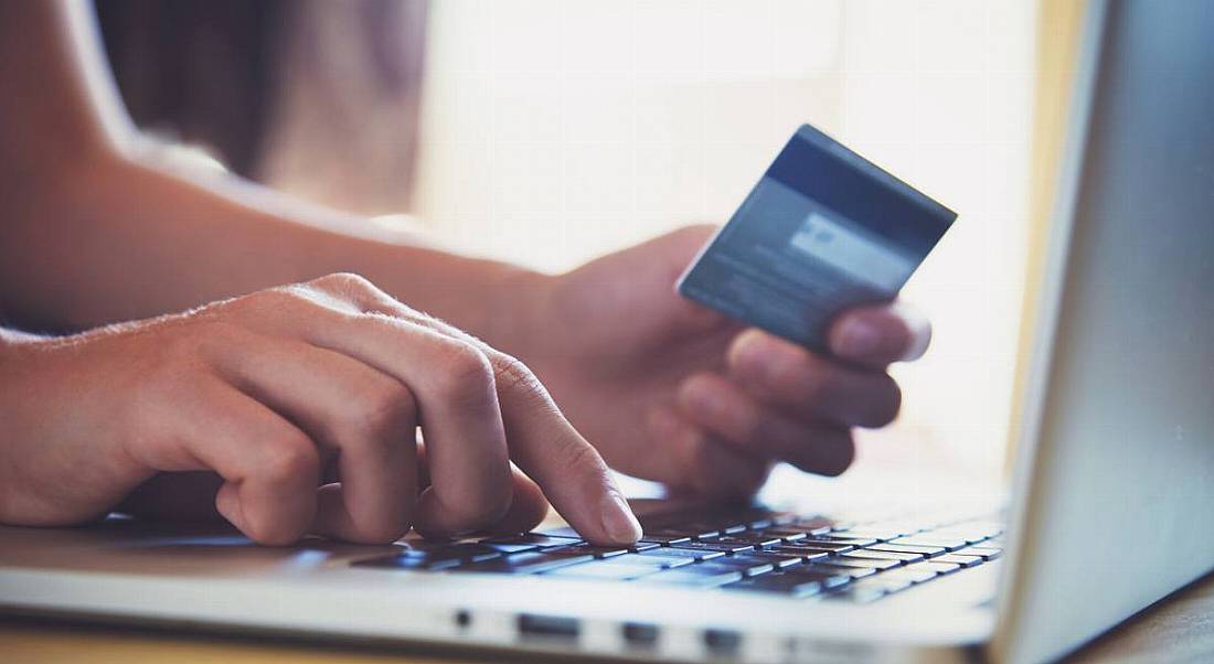 A close-up of a person on a laptop holding a credit card, representing fintech.