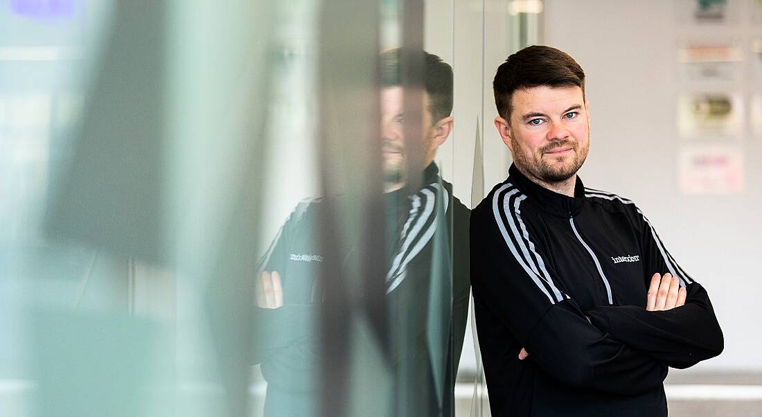 A man in a casual zip-top with Interxion written on it stands cross-armed, leaning against a glass wall.