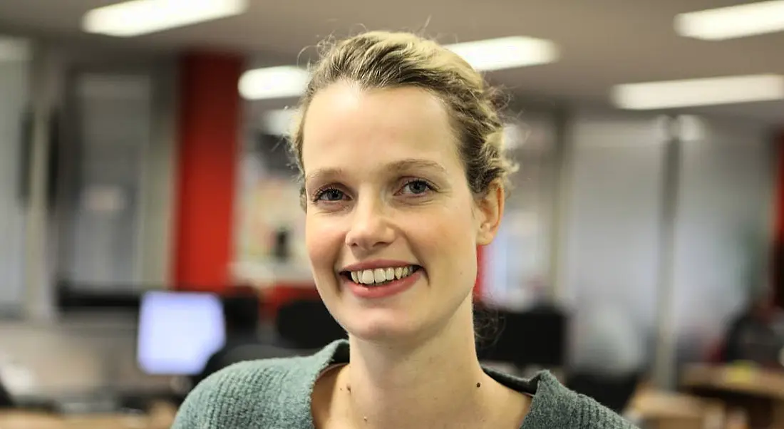 A woman with tied-up blonde hair smiling and wearing a green jumper. She is a software engineer.