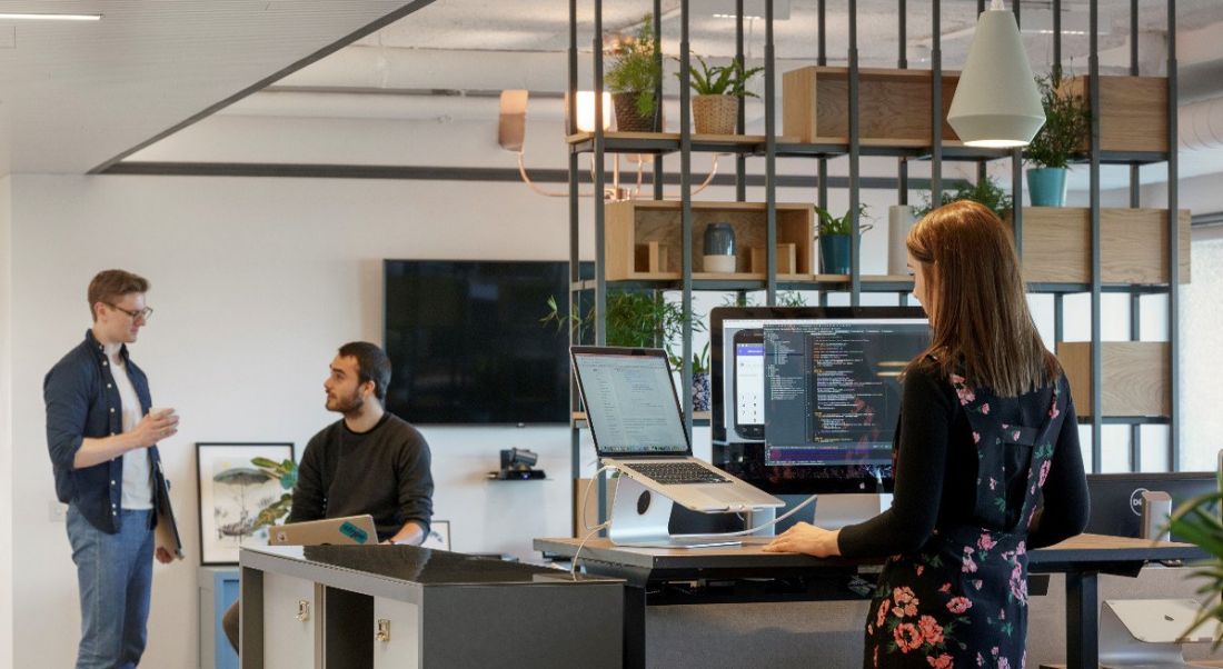 Inside the Stripe offices in Dublin with two male engineers talking and a young woman engineer at work.