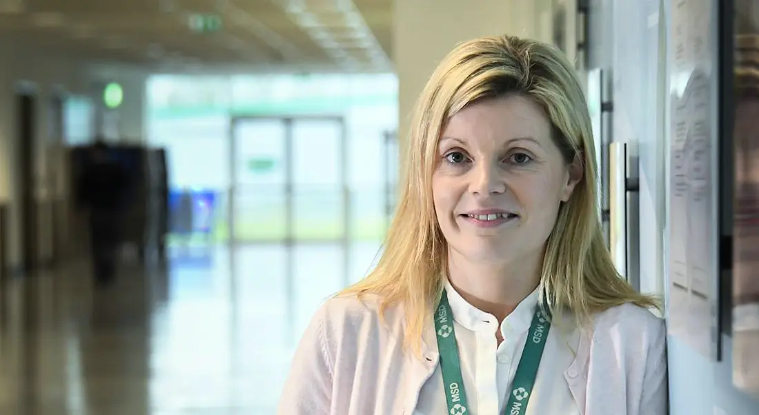 A blonde woman wearing an MSD lanyard looking at the camera in a well-lit hallway.