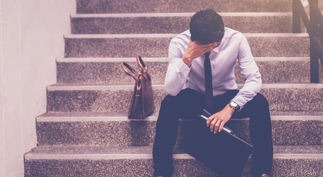 A man sitting on a step with his head in his hand looking very despondent after a bad job interview.