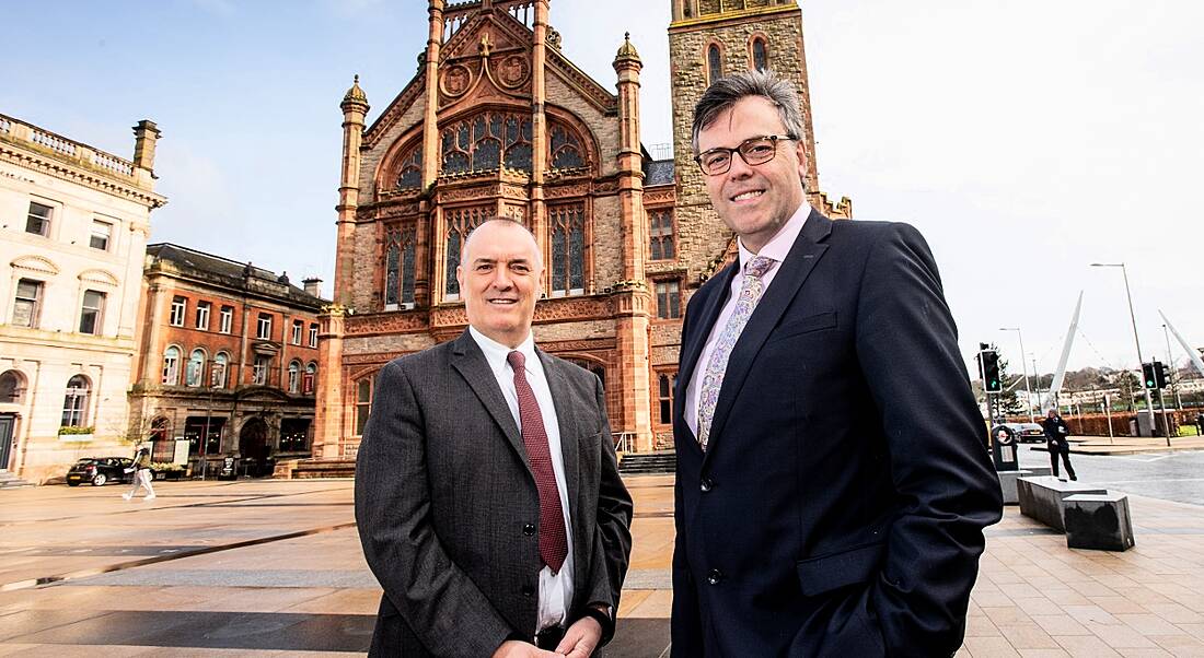 Two men in suits standing outside The Guildhall in Derry, a tall, town hall-style building.