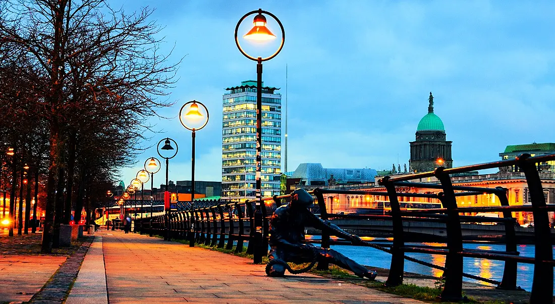 View of Dublin city illuminated at night with brass statue depicting man pulling in fish net near barrier.