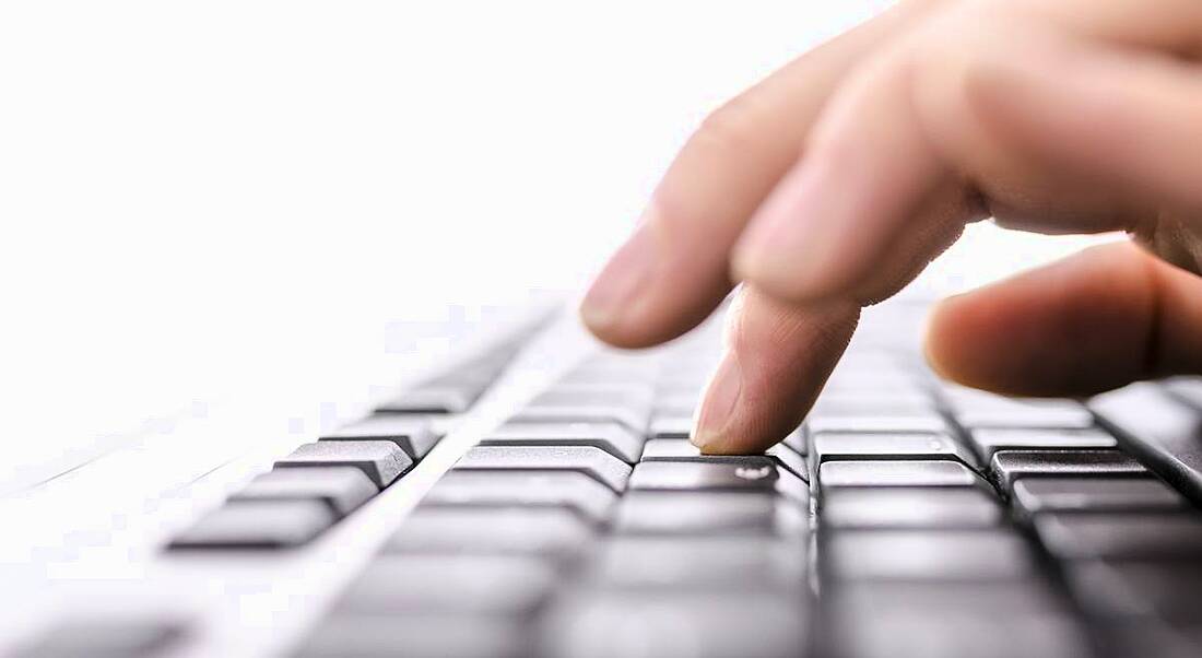 Close-up of a woman’s hands hovering over a laptop keyboard as she types.