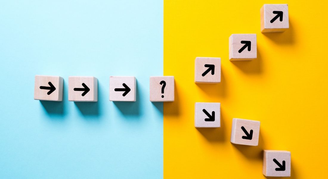 Blue and yellow background with small wooden blocks with arrows drawn on, leading to a question mark block and, from there, splitting into two paths.