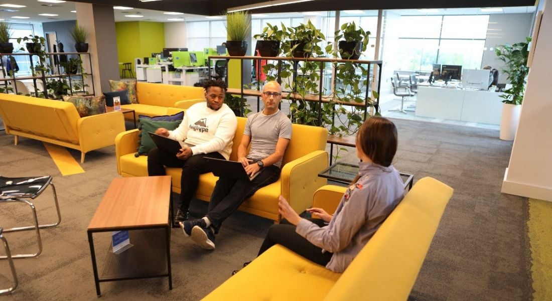 A group of colleagues sitting in a vibrant communal working space, with yellow couches and plants, at Genomics Medicine Ireland.