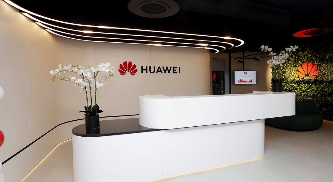 View of lobby of modern white offices with Huawei red lotus logo and the name Huawei written on wall.