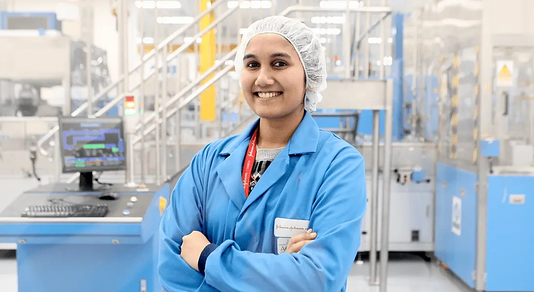 Female professional standing with arms folded in protective laboratory clothing in a lab setting at Johnson & Johnson Vision Care in Ireland.