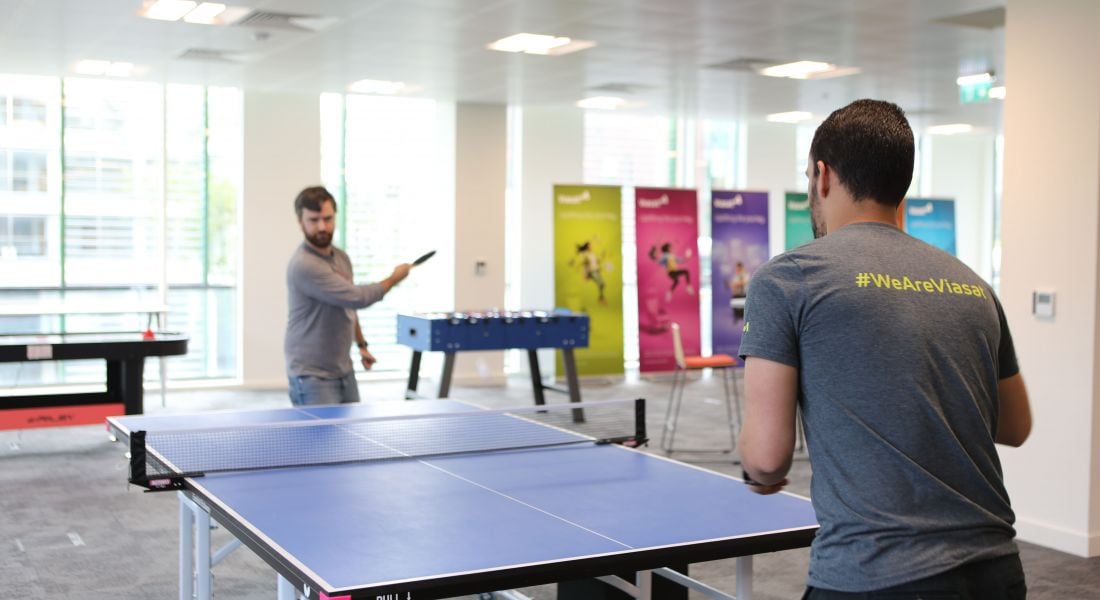 Two colleagues are playing table tennis in a communal office space in Viasat Ireland