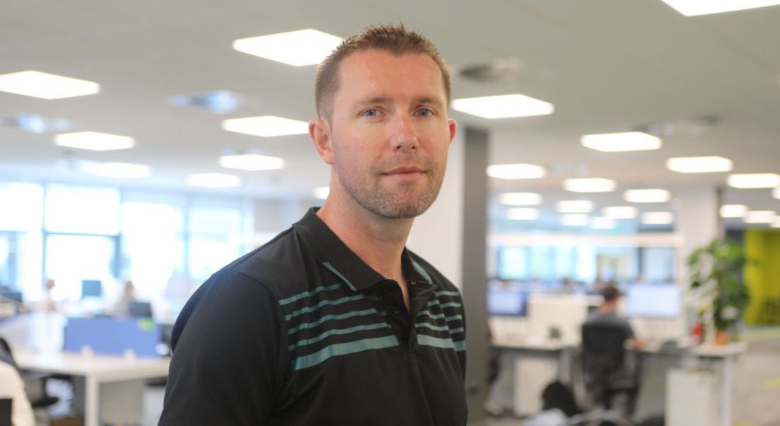 Headshot of a man in casual clothes in an office setting.