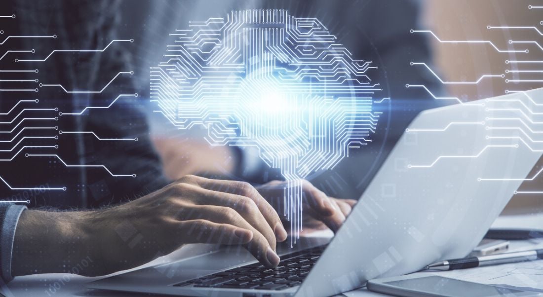 Man typing on laptop keyboard with brain hologram overlaid in the foreground.