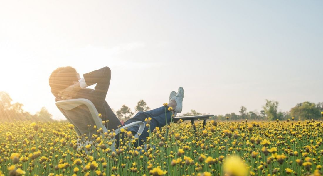 Businessman sitting in office armchair and relaxing in yellow flower field.